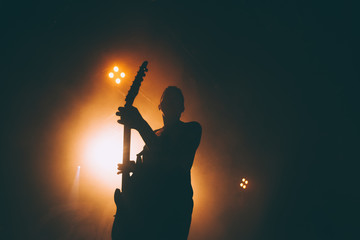 Silhouette of a guitar player in the smoke. The guitarist plays at a rock concert. - obrazy, fototapety, plakaty