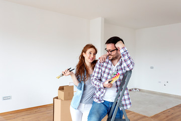 Fototapeta na wymiar Couple in new house plan how to paint walls and looking at samples of colours with brushes on hand
