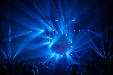 Stage view with blue spotlights. Music show. Silhouettes of the festival. А crowd of fans at the...