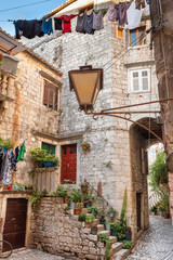 Picturesque narrow street in Trogir city with flower pots and laundry drying