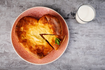 A heart-shaped casserole and a glass of milk on concrete. 