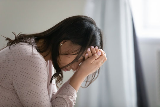 Close up side view African young lonely woman sitting on couch covers face with hands looks desperate. Regret about abortion, break up and divorce, personal life troubles or health problems concept