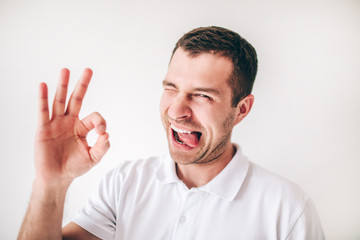 Young man isolated over white background. Emotional funny guy show ok symbol with fingers. Playful man posing alone in studio.