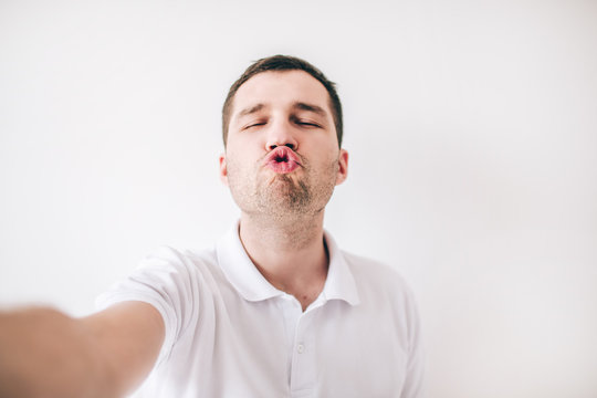 Young man isolated over white background. Ridiculous guy hold lips together like duck. Kissing mode. Funny posing on camera. Hold it with hand.