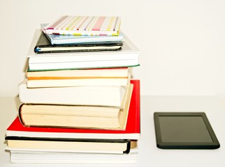 Pile of text books and books next to an e-book