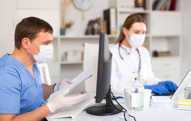 Doctor and nurse in protective mask check patient data in hospital computer database