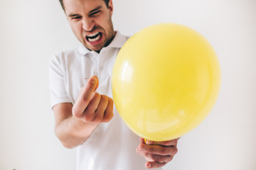 Young man isolated over white background. Guy emotional expressing before piecercing a yellow balloon with needle. Cut view.