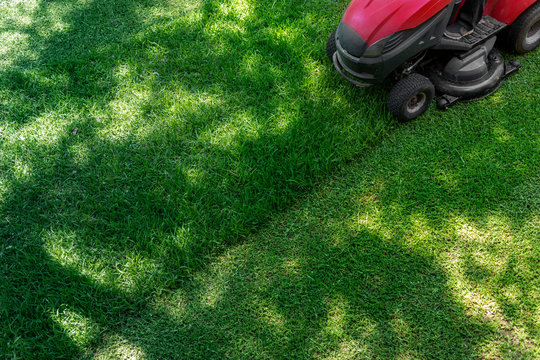Top down above view of professional lawn mower worker cutting fresh green grass with landcaping tractor equipment machine. Garden and backyard landscape lawnmower service and maintenance