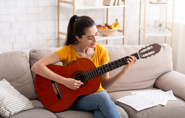 Stay home entertainment. Millennial girl learning to play acoustic guitar in apartment