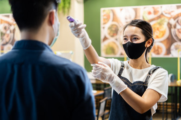 Asian staff restaurant waitress wear protective face mask scan customer temperature by thermometer before entering the restaurant to protect infection from flu fever and coronavirus covid-19