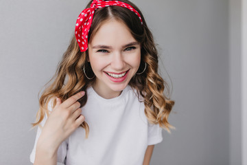 Refined caucasian girl laughing to camera during indoor photoshoot. Amazing good-humoured lady with red ribbon posing in studio.