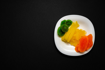 dried fruits lie on a white plate. Black background. Healthy vegetarian food