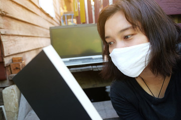 Asian Thai woman wearing a white cloth mask for prevent the Covid-19 or Corona virus serious reading a book for work from home with laptop working online system. Air Pollution Value Pm 2.5 concept.