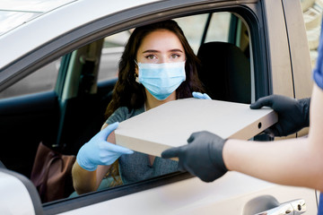 Safe food delivery from pizzeria to car during quarantine covid-19. Attractive young girl in blue...