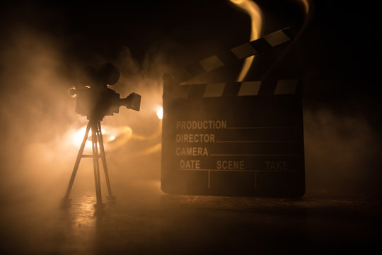 Movie concept. Miniature movie set on dark toned background with fog and empty space. Silhouette of vintage camera on tripod.