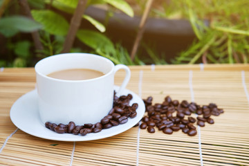 White ceramic cup of hot coffee and beans on Woven mat with natural light morning in the garden. Caffeine drinks cause a fresh feeling.
