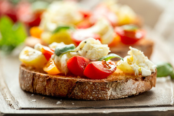 Tomato bruschetta and mozzarella cheese with basil on a rustic wooden board