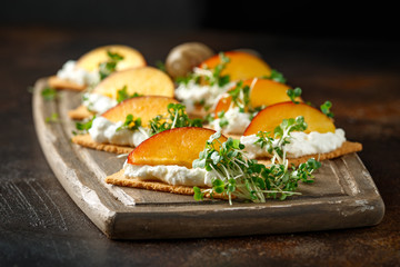 Cottage cheese and nectarine wedges on melba toast appetizers drizzled with runny honey and served with cress salad microgreen. Healthy party finger food