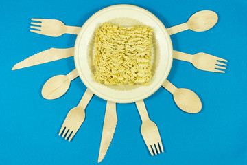 Instant pasta on a colored background with disposable wooden eco cutlery.