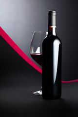 Bottle and glass of red wine on a dark background.