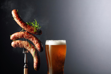 Beer and grilled Bavarian sausages with rosemary. Sausages on a fork sprinkled with rosemary. - obrazy, fototapety, plakaty