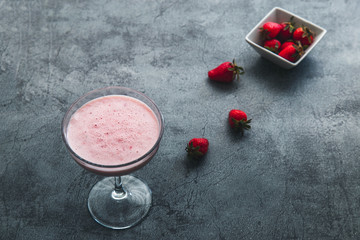 Strawberry smoothie and strawberries over rustic stone backdrop with dramatic dark lighting