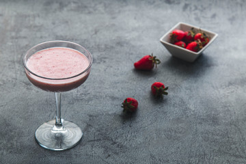 Strawberry smoothie and strawberries over rustic stone backdrop with dramatic dark lighting
