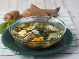 A bowl of spring natural soup made of herbs and shavel on a white wooden table with homemade wholegrain bread.Sorrel soup.