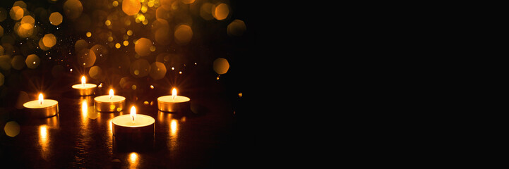 Several burning candles with festive bokeh on a black background. Banner with copy space.