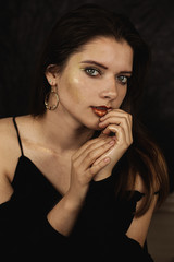 portrait of a young girl with gold makeup in black clothes on a black background