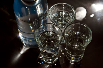 Glasses with alcohol near the bottle. Transparent drink on a black background. Blue reflexes on the bottle.