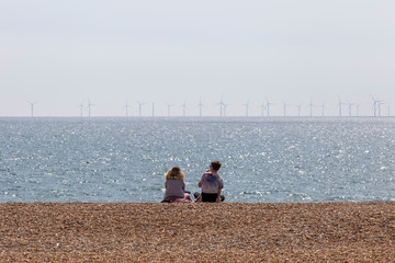 couple sitting on beach with wind farm