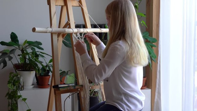 stay at home. work during the quarantine - a girl in the living room mural weaving of the ropes in the macrame technique