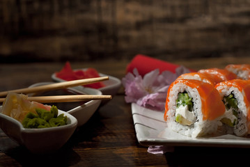 Sushi on a white plate. Sushi roll with sauce and spices on a black background. Food on a wooden table with dark boards. Sakura color on a plate. Flower with rose petals.