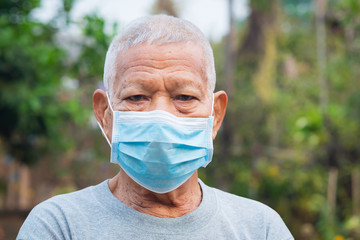 A portrait of an elderly man wearing a face mask looking at camera while standing in a garden. Mask for protect virus, coronavirus, pollen grains. Concept of old people and healthcare - Powered by Adobe