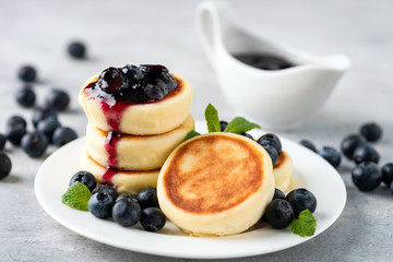 Syrniki or cottage cheese fritters with blueberry jam on white plate. Traditional Russian and Ukrainian breakfast or lunch food, sweet cheese pancakes served with berry sauce