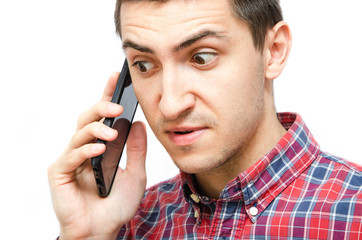 Young man in a plaid shirt with a smartphone on a white background. The guy holds a smartphone by the ear, talking on the phone. Anger, anger, surprise, attentiveness during a telephone  conversation
