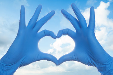 Heart build doctor hands in medical surgical gloves on sky clouds background