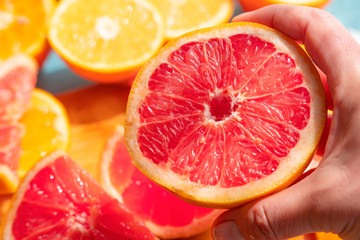 Macro and focus on one round shaped grapefruit in the center of oranges slices. Hand holding freshly cut grapefruit slice