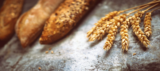 Fresh bakery food. Crusty loaves of mixed breads and buns and ears of wheat on rustic table...