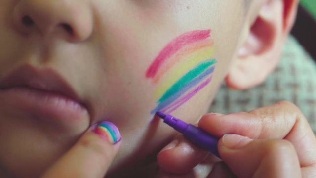 Close-up view of a little boy. LGBTQ parent painting rainbow flag on cheeks. Pride day 2020, LGBT family, gender rights and equality concepts