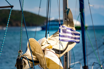 Small greek flag flying on a sailing boat lying in a mediterranean harbour on a sunny summer day.