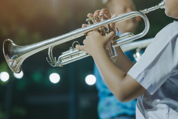 Male student with friends blow the trumpet with the band for performance on stage at night.