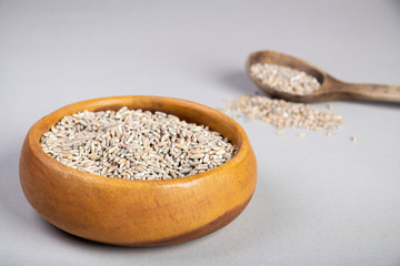 Unpeeled raw oats in a wooden plate on a Gray background