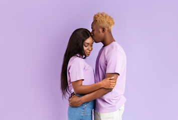 Millennial black guy hugging and kissing his girlfriend on lilac background