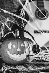 Black and white,  slightly blurred photo with strong grain effect. Laughing pumpkin in headphones with guitar in the background. Halloween,  artistic concept.