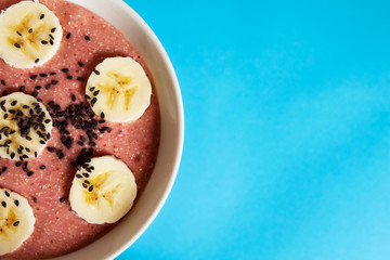 Banana and strawberry smoothie bowl on a blue background with copy space