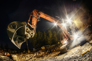 Orange excavator digger working at night on the street
