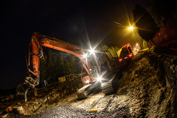Orange excavator digger working at night on the street
