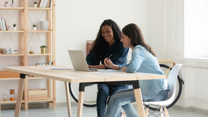 Happy young african american businesswoman talking with laugh female mentor in coworking boardroom...